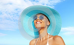 Happy young woman at the beach side, wearing a turquoise sun hat, blue sunglasses and bikini, portrait of African latin American