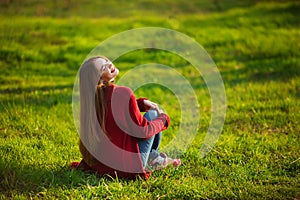 Happy young woman. Beautiful female with long healthy hair enjoying sun light in park sitting on green grass. Spring