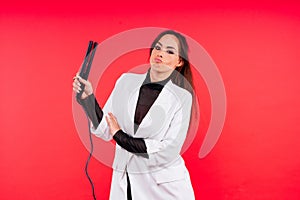 Happy young woman with beautiful hair holding curling iron on grey and red background