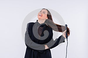 Happy young woman with beautiful hair holding curling iron on grey and red background