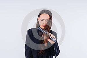 Happy young woman with beautiful hair holding curling iron on grey and red background