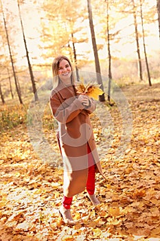 Happy young woman in a beige coast walks outdoors in autumn park, concept autumn.