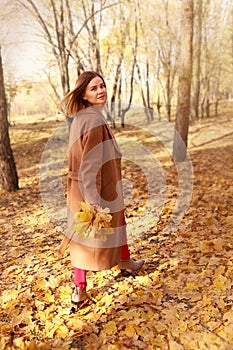 Happy young woman in a beige coast walks outdoors in autumn park, concept autumn.