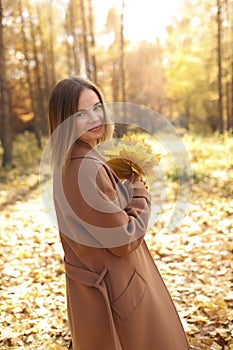 Happy young woman in a beige coast walks outdoors in autumn park, concept autumn.