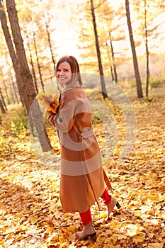 Happy young woman in a beige coast walks outdoors in autumn park, concept autumn.