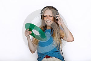 Happy young woman in big black professional dj headphones holding trendy green colorful vinyl record posing against white studio b