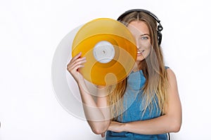 Happy young woman in big black professional dj headphones holding trendy yellow colorful vinyl record posing against white studio