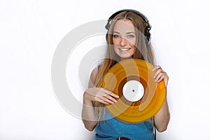 Happy young woman in big black professional dj headphones holding trendy yellow colorful vinyl record posing against white studio