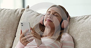 Happy young woman in big wireless pink headphones using smartphone