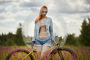 Happy young woman with bike in a summer flower field