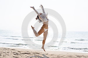 Happy young woman in bikini jumping on the beach