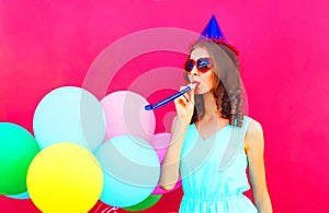 Happy young woman in a birthday cap with an air colorful balloons over pink background