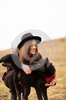 Happy young woman with black hat, plaing with her black dog on the shore of the lake