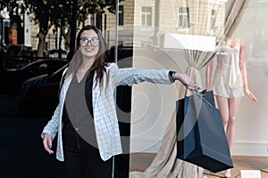 Happy young woman with black shopping bag on shop window background. Girl student after shopping with bag in her hands