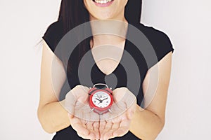 Happy young woman in black t-shirt a holding red alarm clock and waving hand