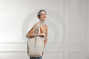 Happy young woman with blank eco friendly bag near white wall. Space for text
