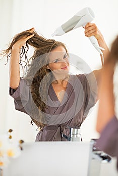 Happy young woman blow drying hair in bathroom