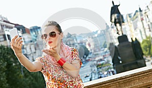 Happy young woman blowing air kiss and taking selfie in Prague