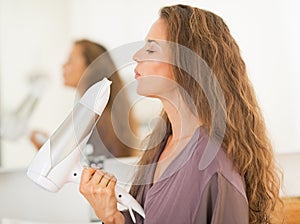 Happy young woman blowing on blow dryer