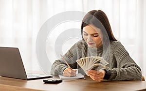 Happy young woman budgeting with cash and calculator at desk