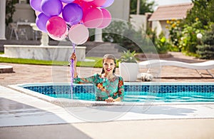 Happy young woman a bunch of balloons after jumping into a swimming pool in a dress.