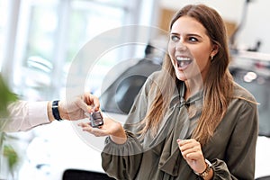 Happy young woman buying car in showroom