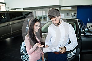 Happy young woman buying a new car at vehicle showroom