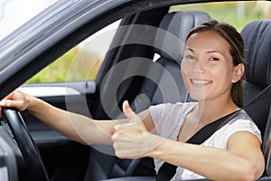 Happy young woman in car with thumbs up