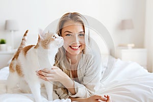 Happy young woman with cat in bed at home