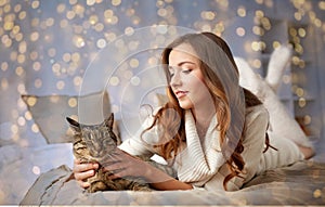 Happy young woman with cat lying in bed at home
