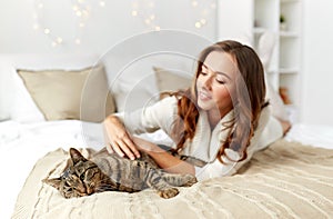 Happy young woman with cat lying in bed at home