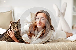 Happy young woman with cat lying in bed at home