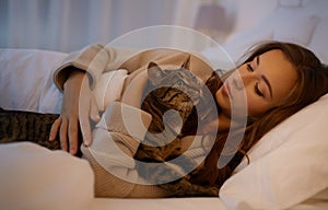 Happy young woman with cat lying in bed at home