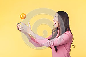 Happy young woman catching falling mandarin isolated on yellow background