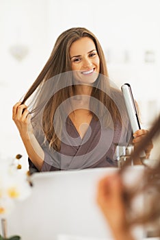 Happy young woman checking hair after straightening