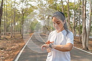 Happy young woman checking her run time on her smart watch after morning run at a local running park