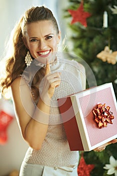 Happy young woman with Christmas gift showing shh gesture