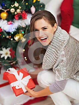 Happy young woman with christmas present box near christmas tree