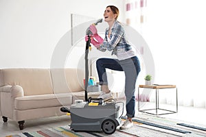 Happy young woman cleaning home with vacuum cleaner and having fun