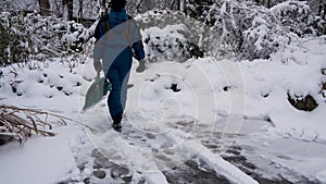 Happy young woman cleans snow in the garden near the house. Portrait of a girl with a snow shovel in her hands. Happy girl removes