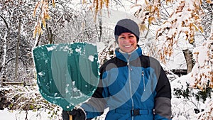 Happy young woman cleans snow in the garden near the house. Portrait of a girl with a snow shovel in her hands. Happy girl removes