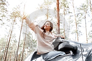 Happy young woman climbed out of a car window. Traveling by car in the forest. Country trip. Vacation by car