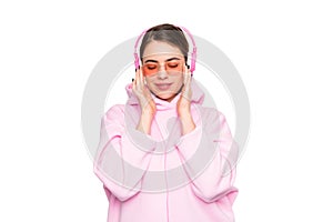 Happy young woman with closed eyes in pink glasses and hoodie enjoy listening to music in headphones