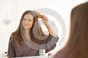 Happy young woman combing hair in bathroom