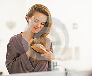 Happy young woman combing hair in bathroom