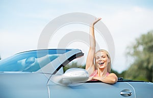 Happy young woman in convertible car waving hand