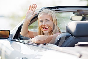 Happy young woman in convertible car waving hand