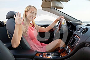 Happy young woman in convertible car waving hand