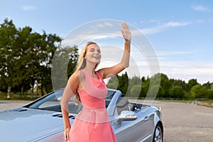 Happy young woman in convertible car waving hand