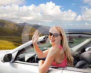 Happy young woman in convertible car waving hand